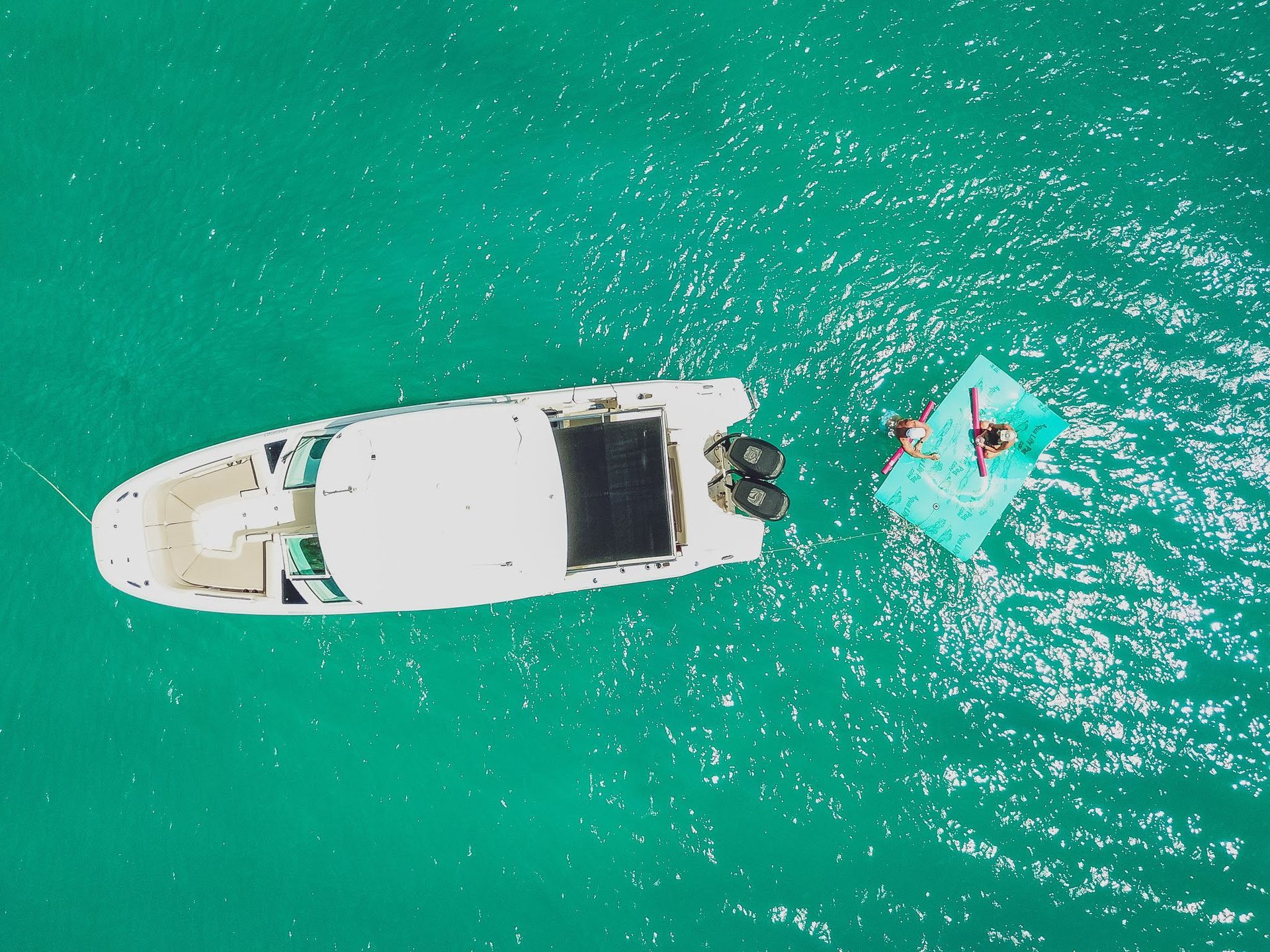 An aerial view of a boat and a person floating on a raft in the ocean.