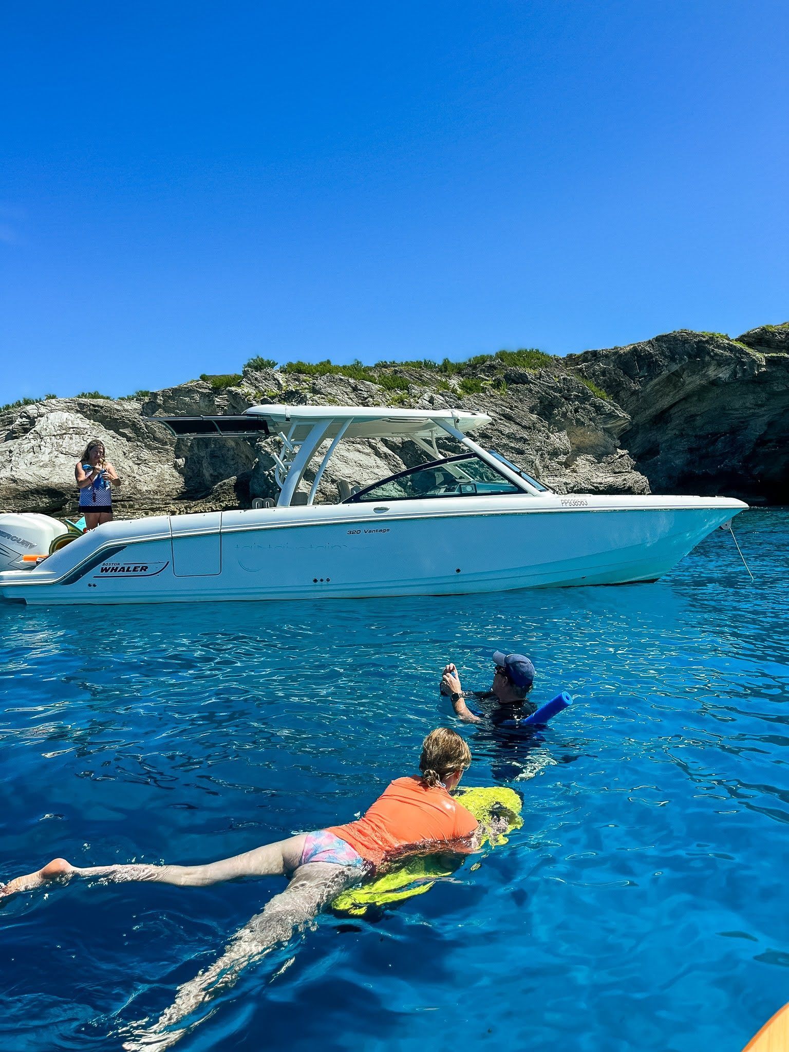 A woman is laying on a surfboard in the ocean next to a boat.