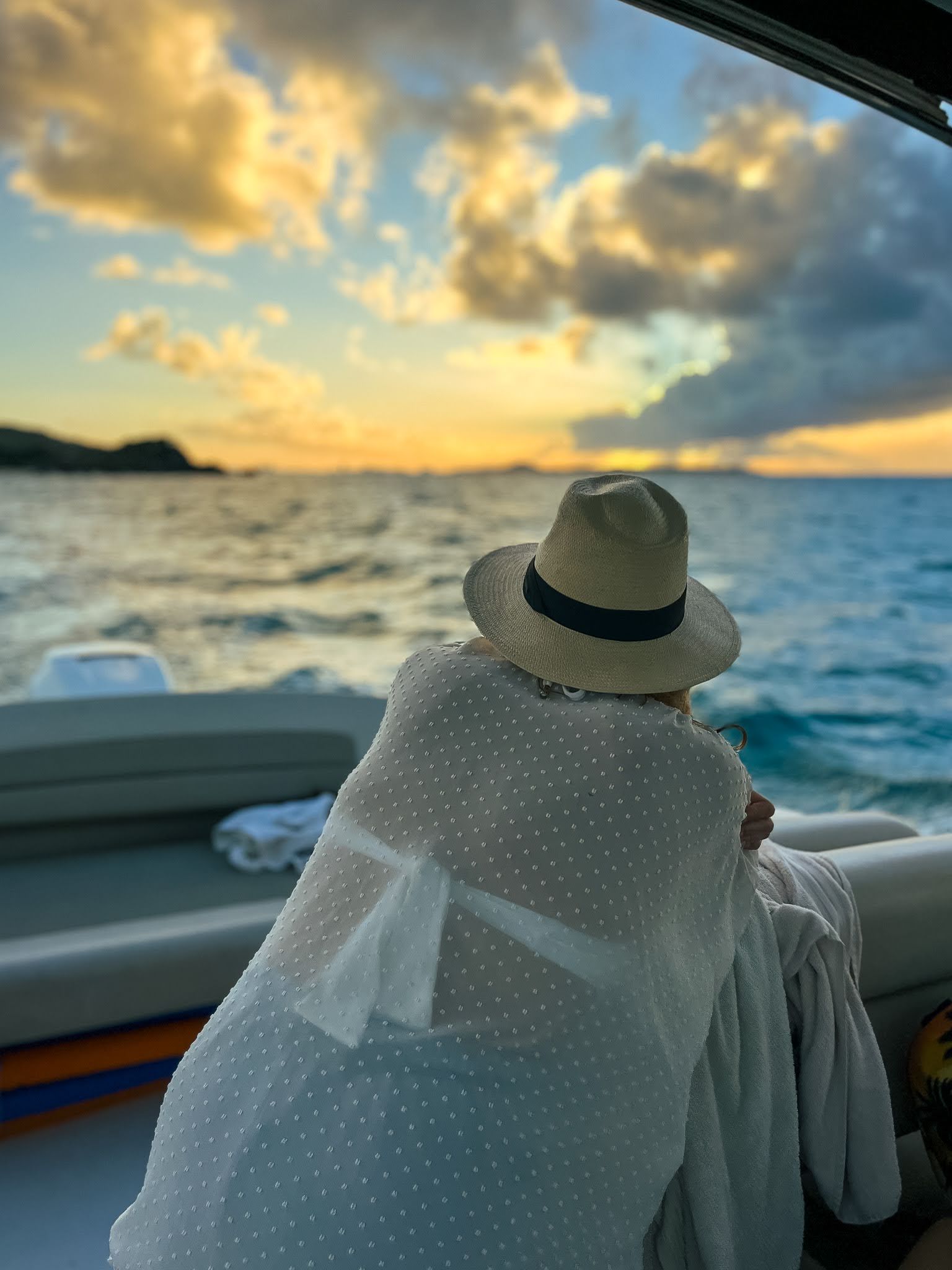 A woman in a hat is sitting on a boat looking at the ocean.