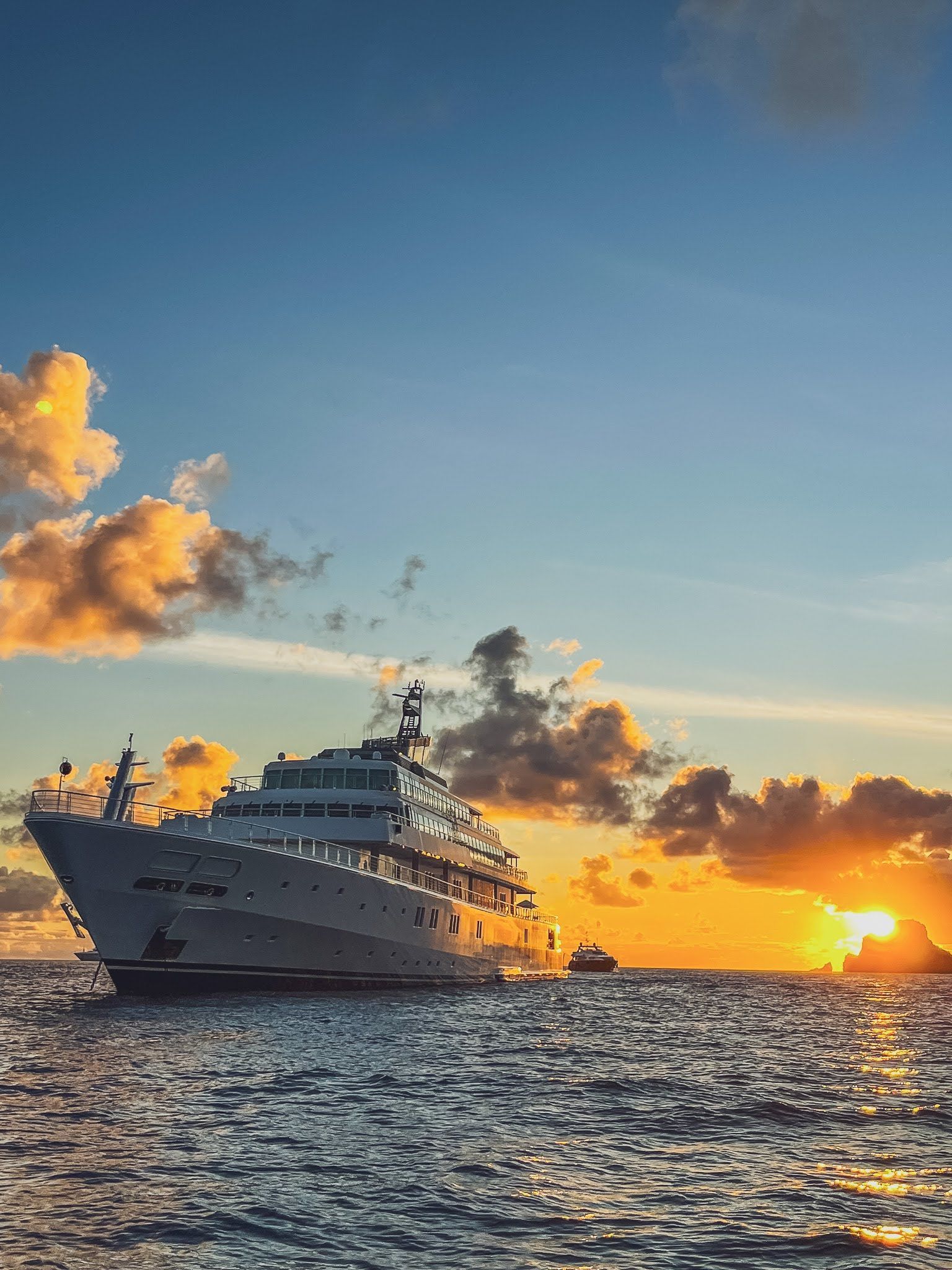 A large cruise ship is floating on top of a large body of water at sunset.
