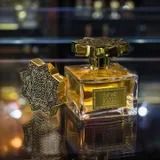 Flacone di profumo dorato su una superficie riflettente, con tappo dorato testurizzato e luci sfocate sullo sfondo.