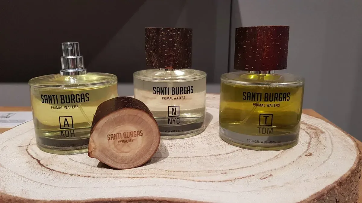 Tre flaconi di profumo su una lastra di legno, con una fetta di legno rotonda davanti.