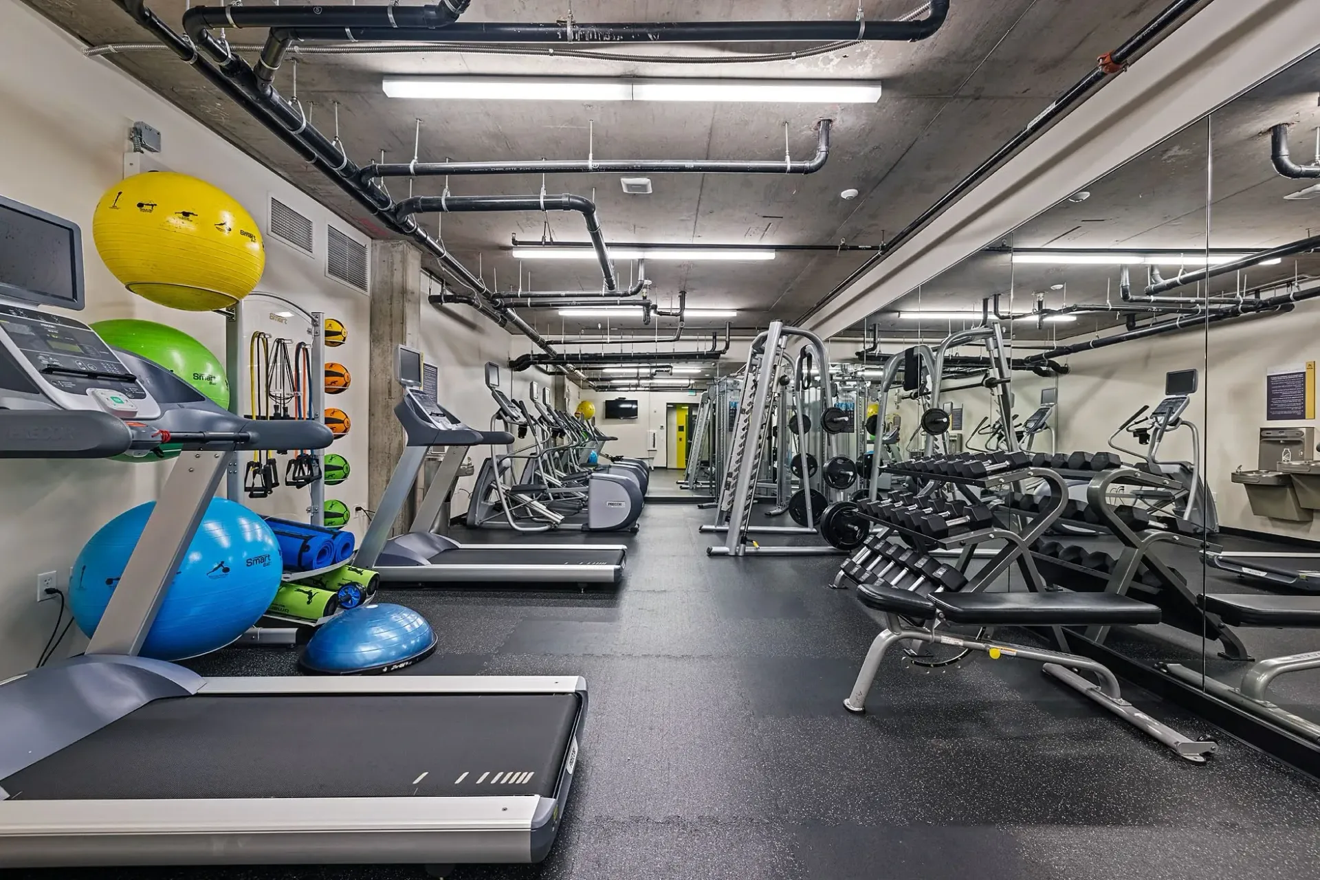 Fitness center with treadmills, elliptical machines, weight machines, and dumbbells.