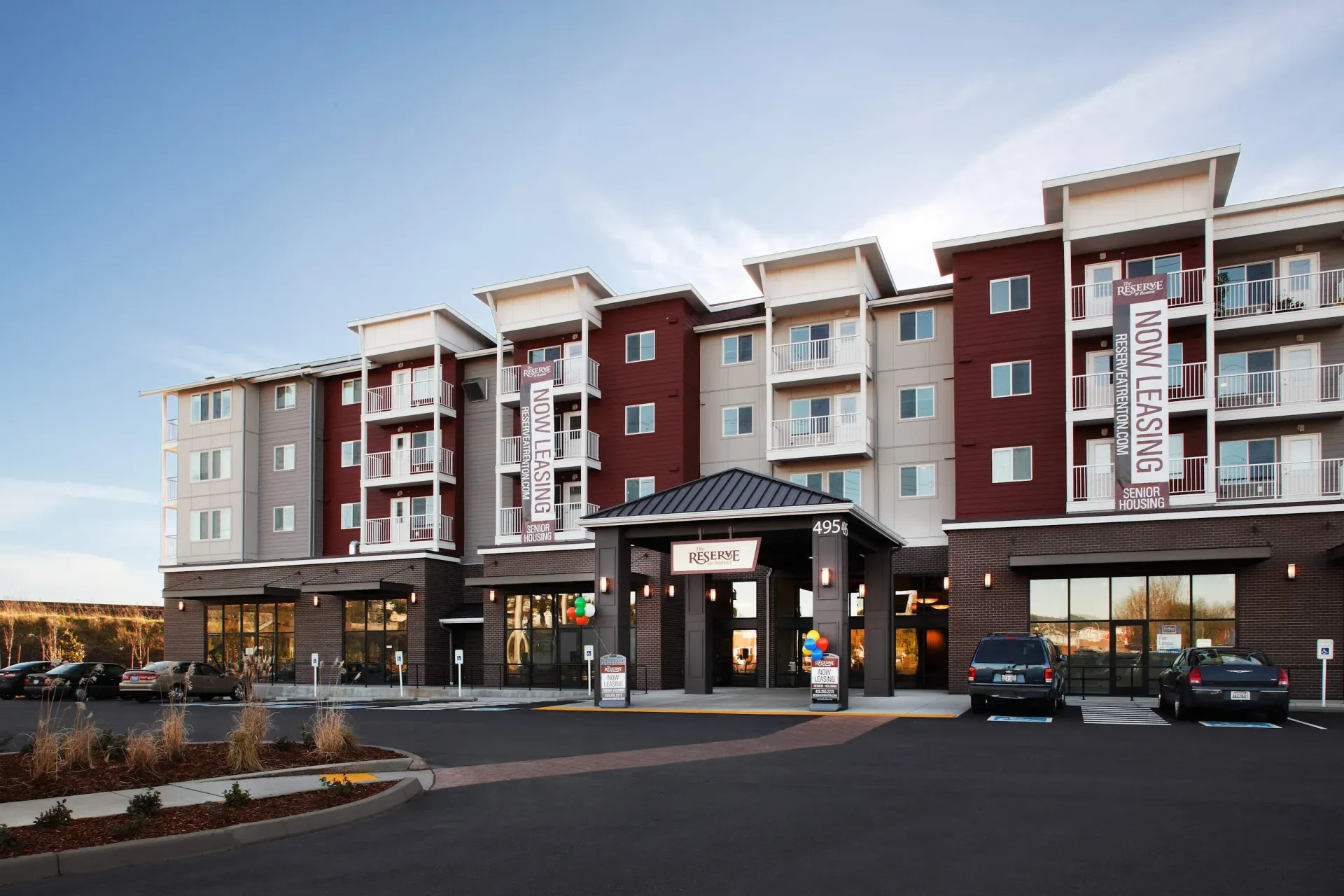 Exterior view of a modern apartment complex with a central entry canopy and leasing banners.