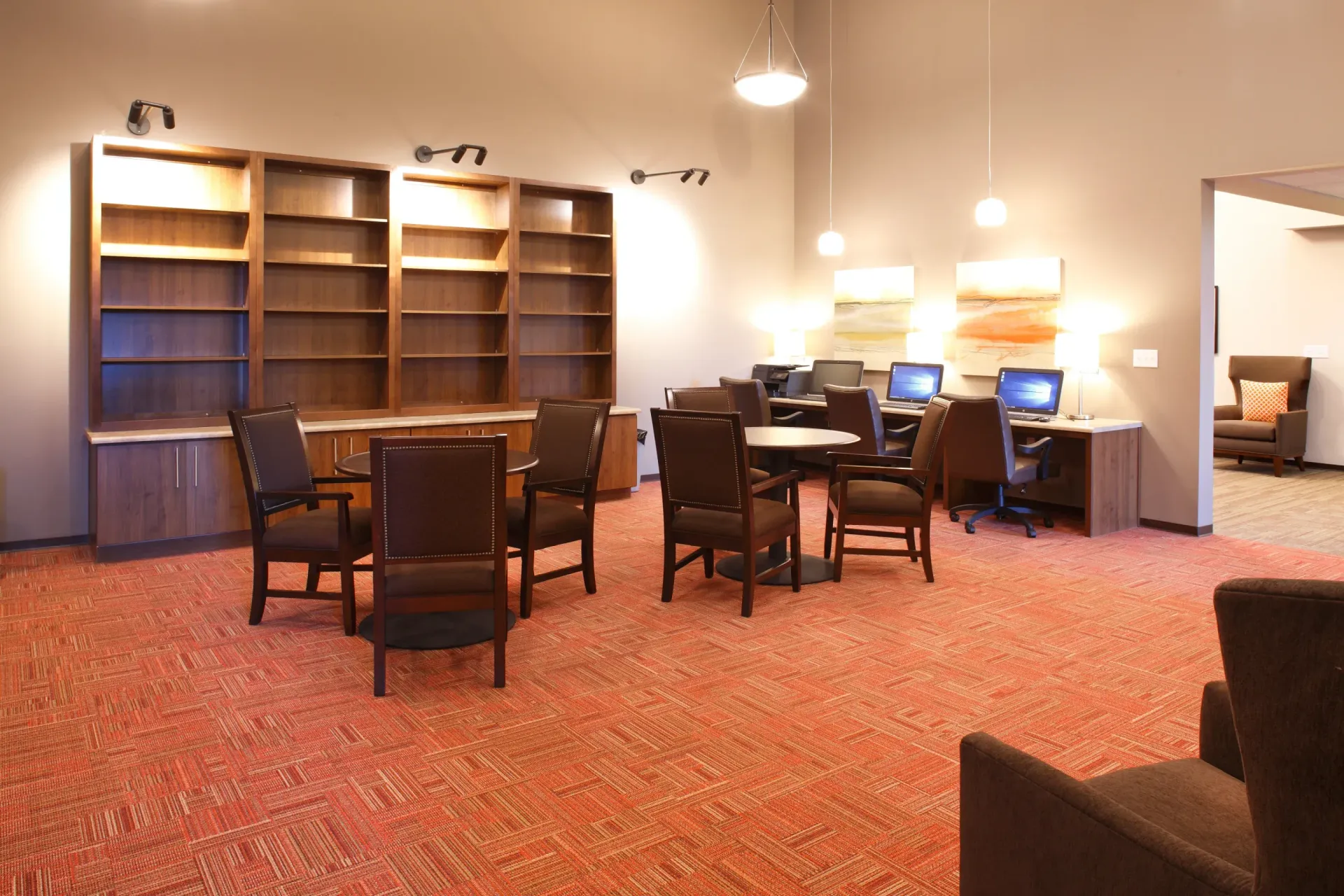 Interior common lounge with work desks, computers, and brown chairs under warm lighting.