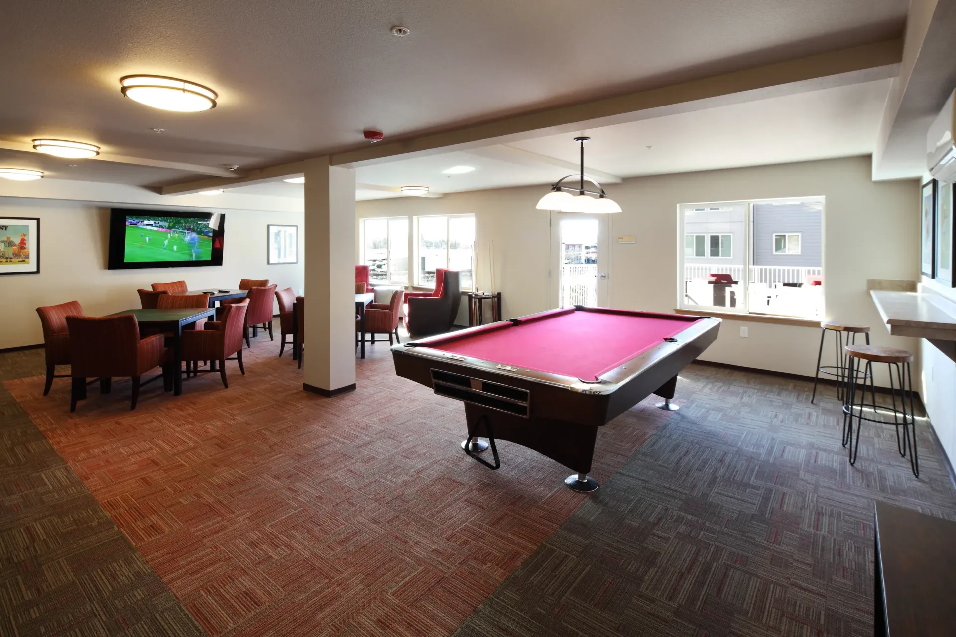 Communal amenity lounge with a red-felt pool table, seating groups, and a wall-mounted TV.