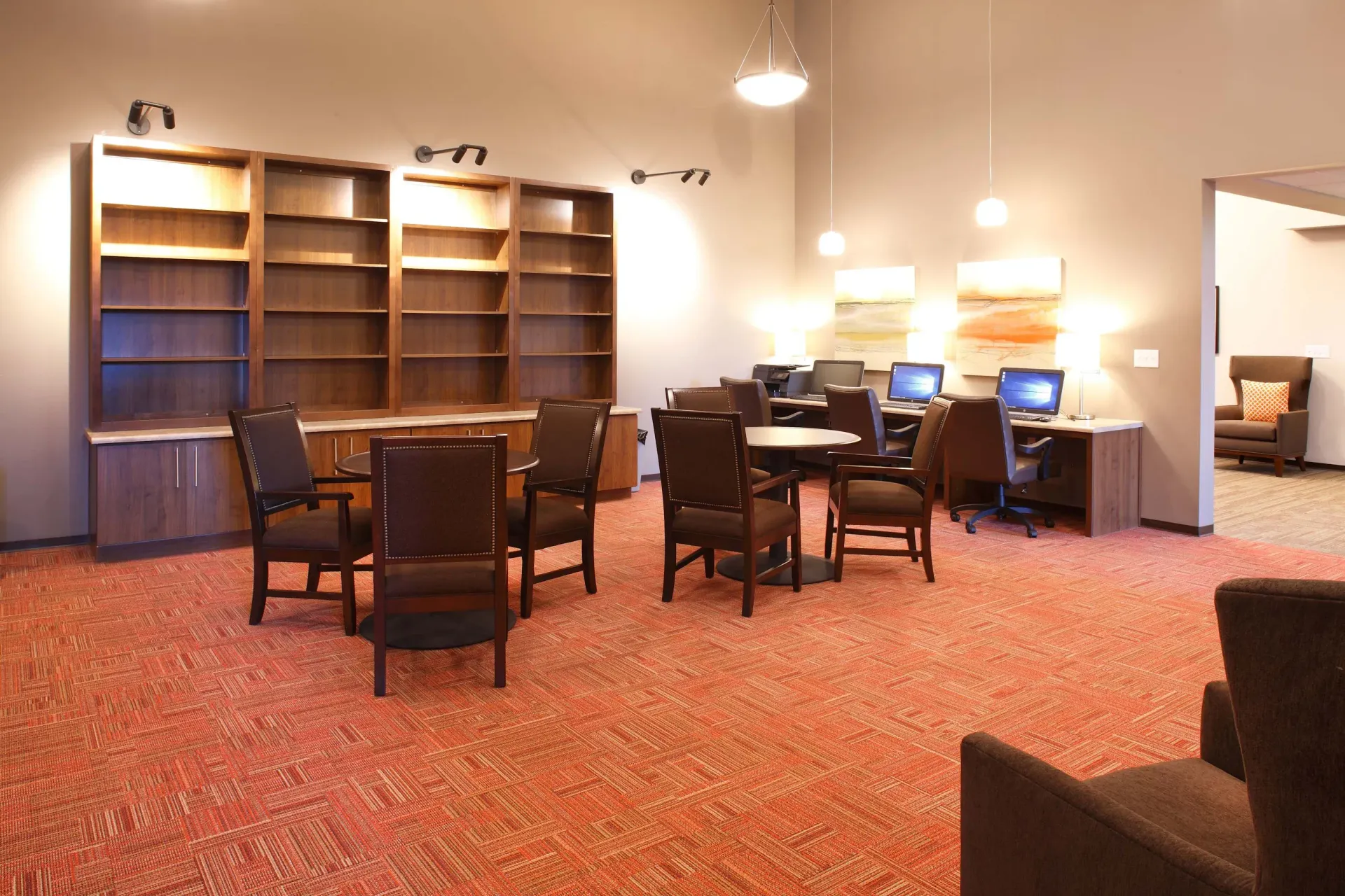 Common area with desks, computers, and lounge chairs in a warm, well-lit room.