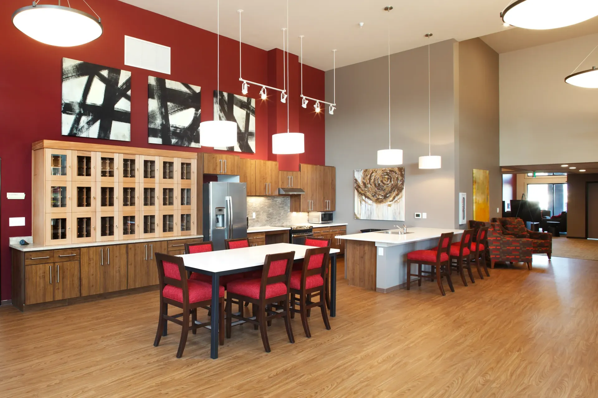 Open communal kitchen and lounge area with wood cabinets, island, and red chairs.