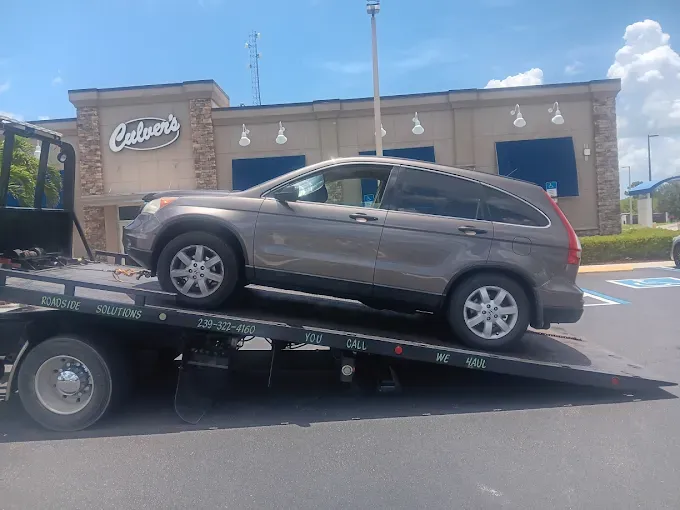 A brown SUV loaded onto the flatbed of a tow truck in front of a Culver's restaurant.
