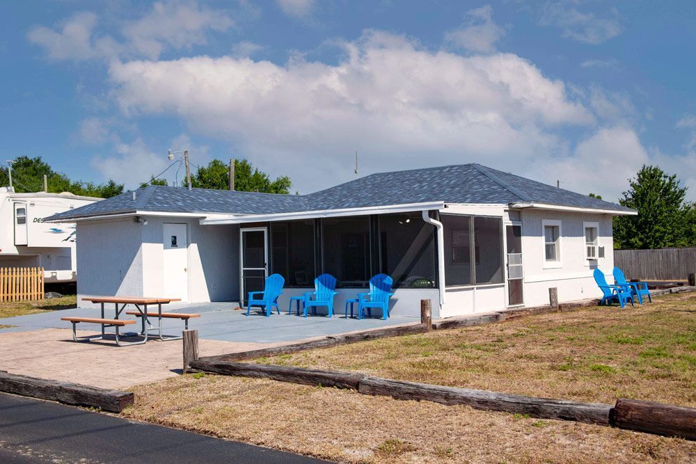 White beach house with screened porch, blue chairs, picnic table, and blue painted patio.