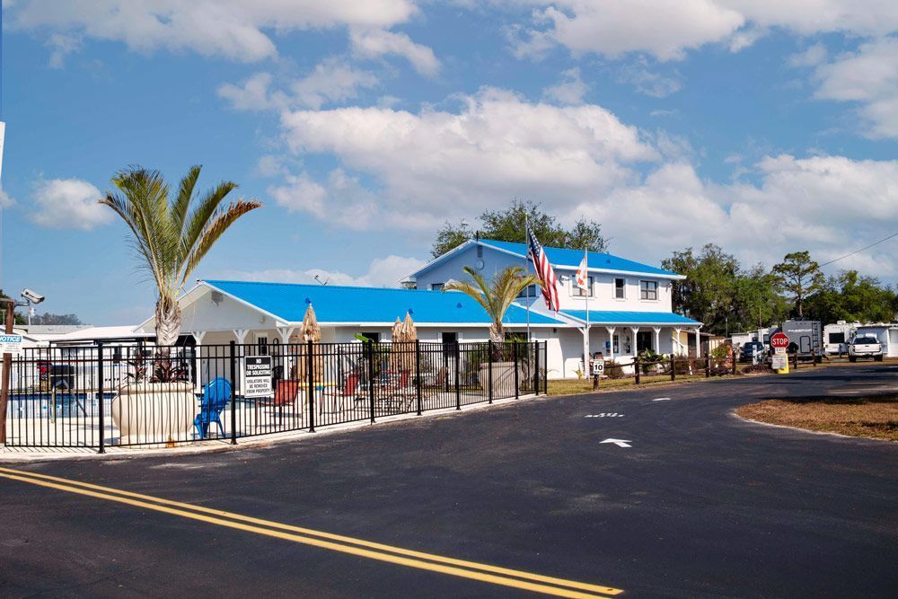 A white building with a blue roof and American flag, pool and palm trees under a blue sky.