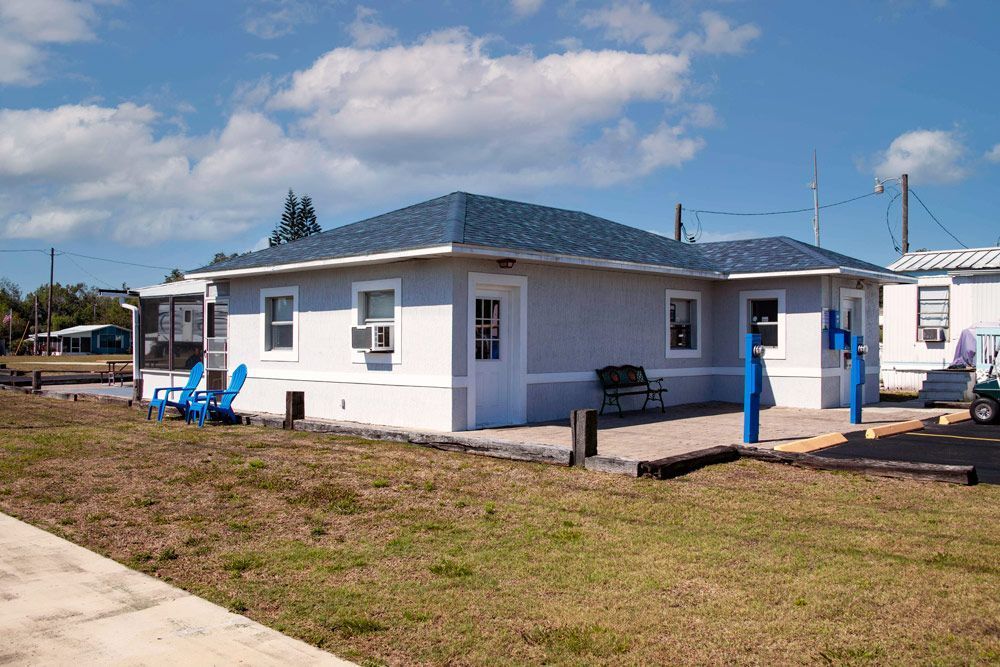 Blue-roofed, light blue house with white trim. Adirondack chairs on a porch. Sunny day, grassy lawn.