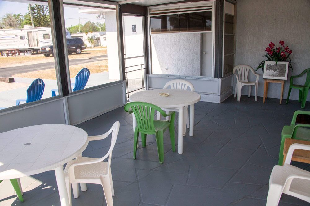 Enclosed patio with white tables, plastic chairs, and flowers. RVs are visible through the windows.