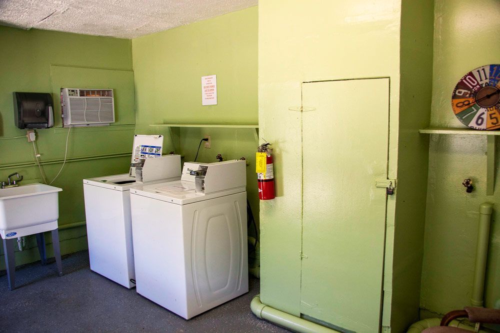 Laundry room with two white washing machines, sink, and storage cabinet; green walls and fire extinguisher.
