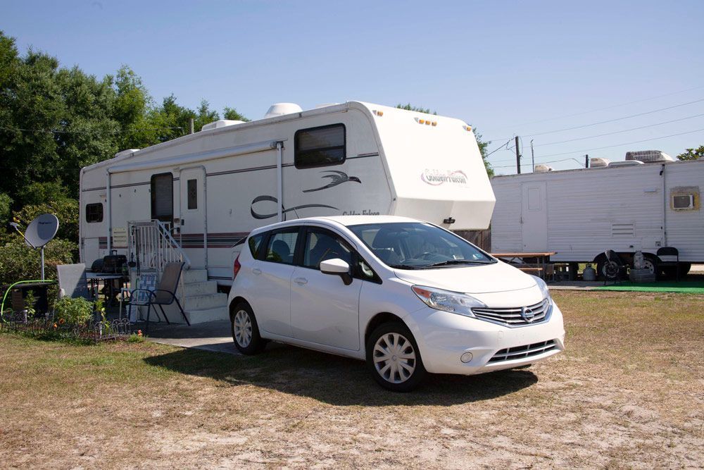 White car parked in front of a white RV. Sunny day, outdoors.