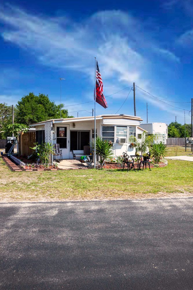 Small white house with American flag on a sunny day. Green lawn, blue sky, and a black road.