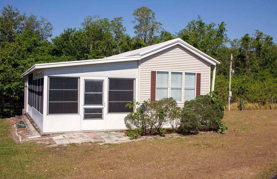 Small beige house with screened porch, two windows, and brown shutters, on a grassy lot.