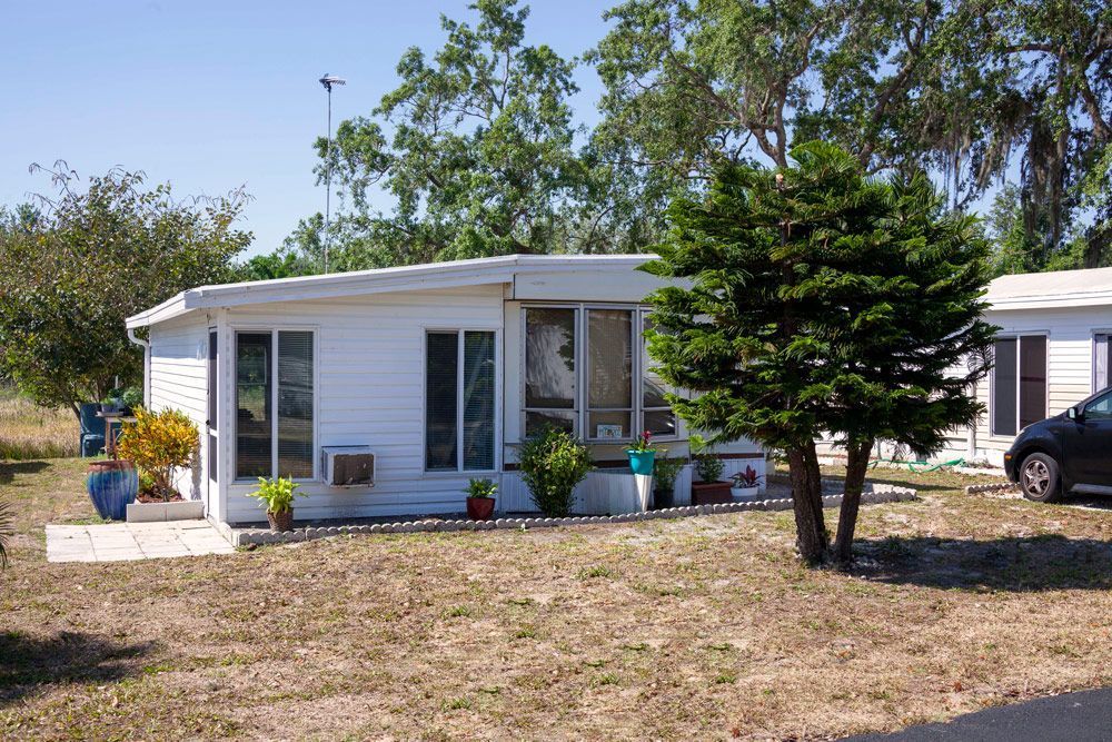 White mobile home with small tree in front on a sunny day.