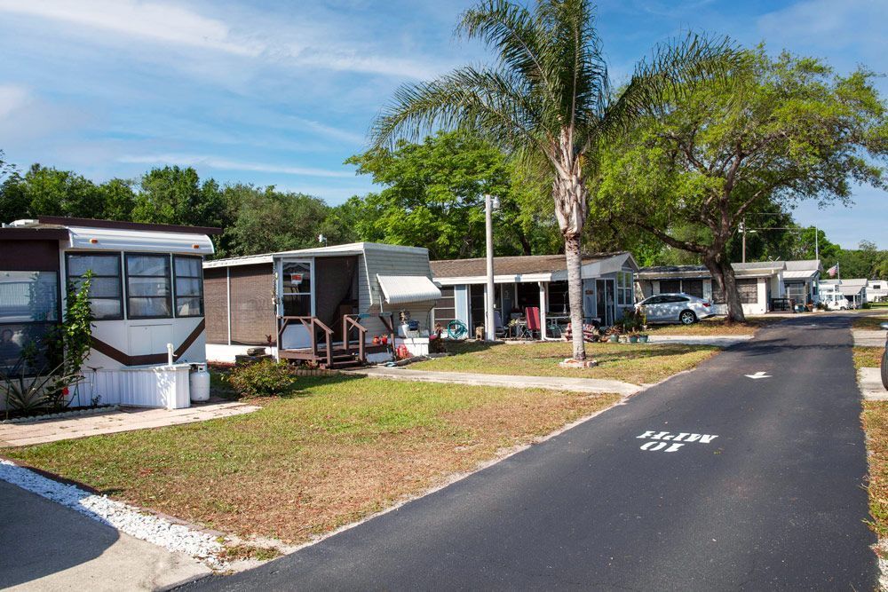 Mobile homes along a paved road, on a sunny day. Green grass and trees line the road.