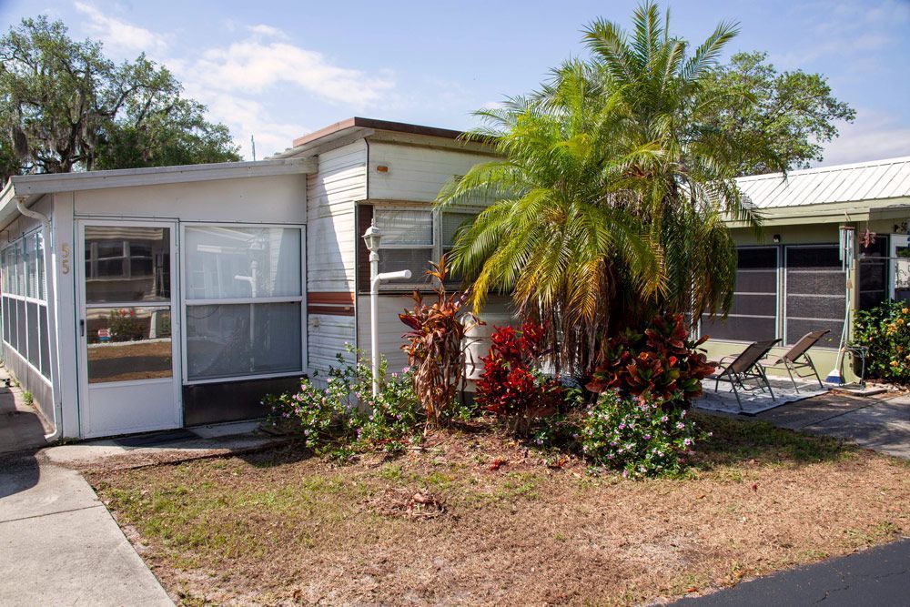 Mobile home with sunroom, palm tree, and landscaping on a sunny day.