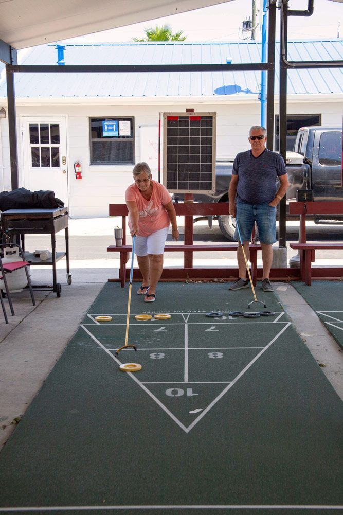 Two people playing shuffleboard outdoors, aiming pucks at a numbered triangular target.