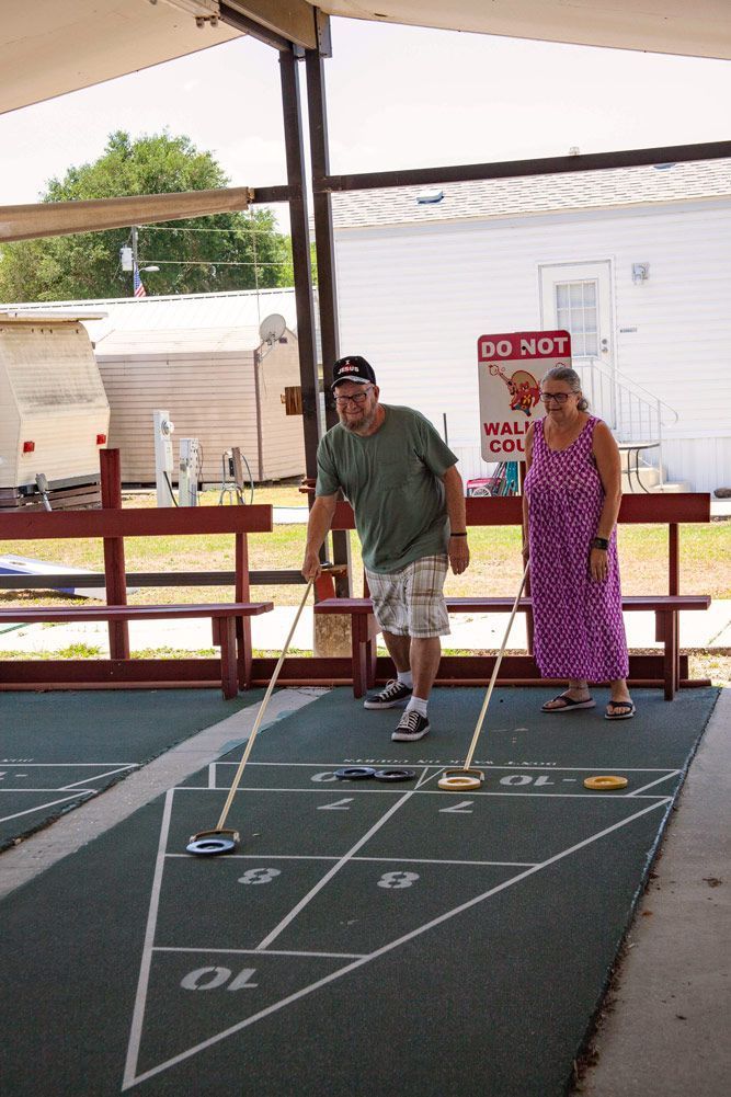 Two people playing shuffleboard outdoors, aiming pucks at targets.
