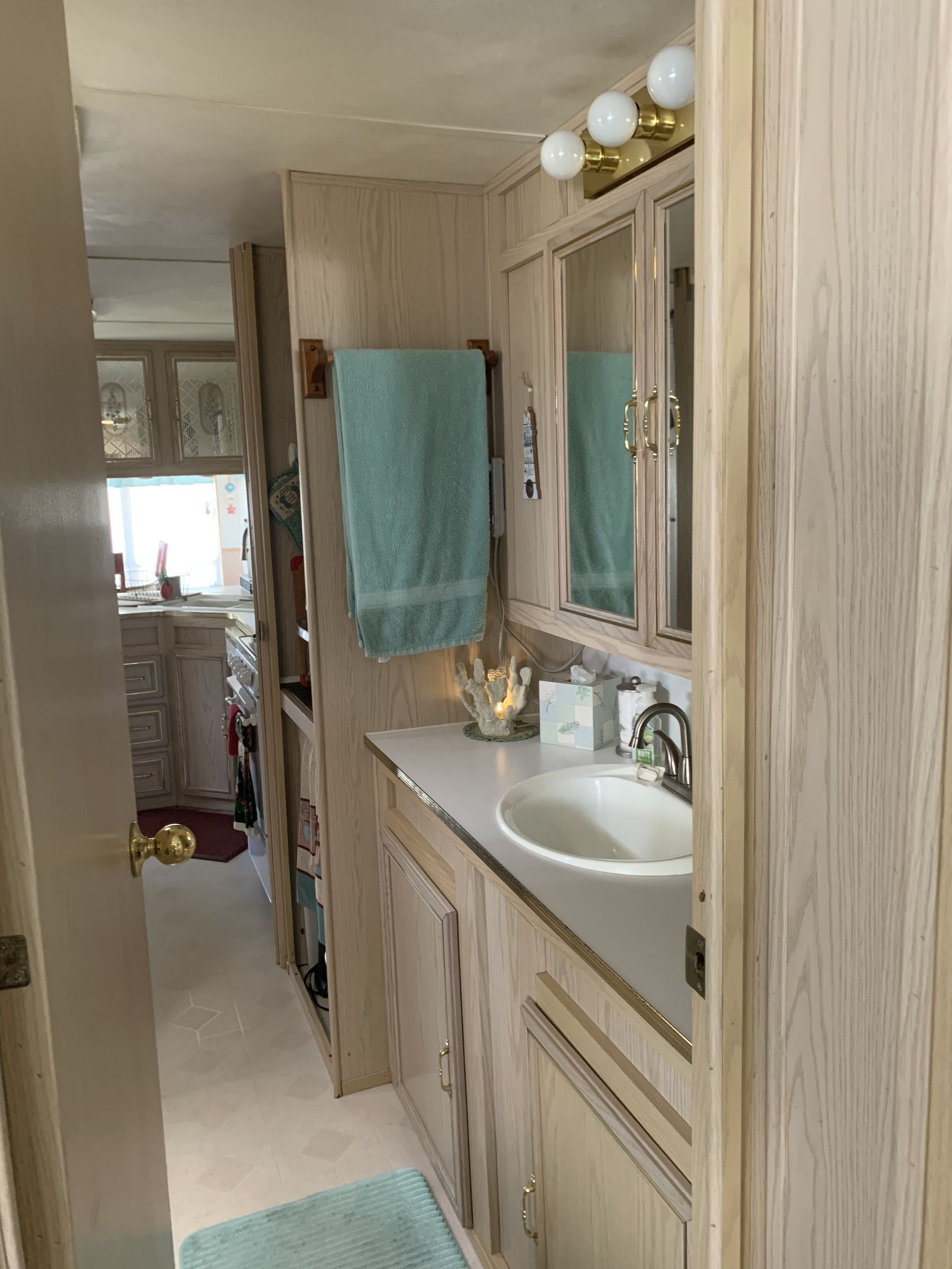 Narrow RV bathroom, light wood paneling, turquoise towel, sink, vanity, mirror.