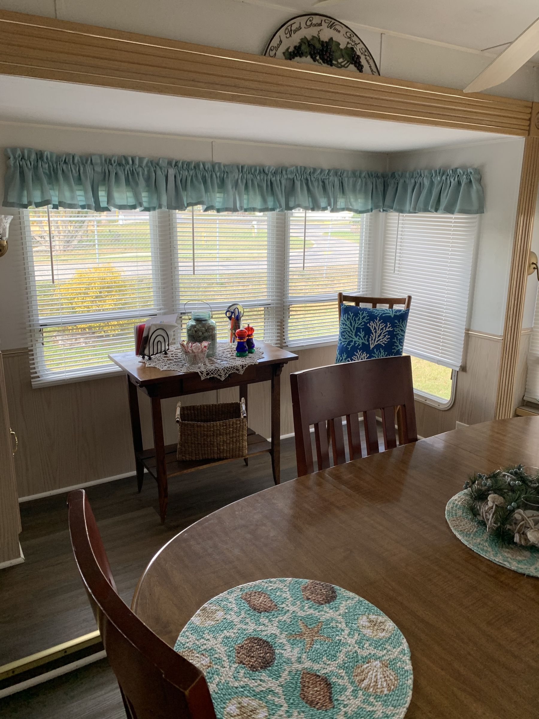 Dining area with table set for a meal; window with valance, table with decor, wooden chairs and blinds.