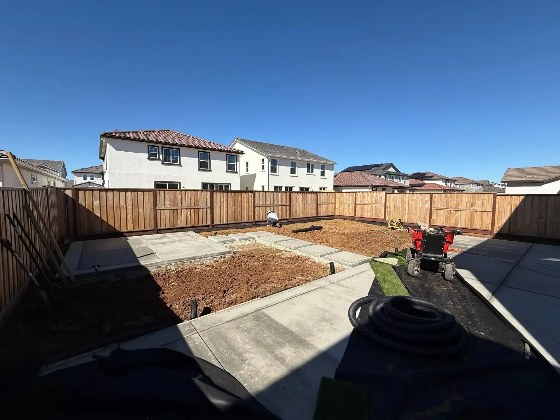 Backyard with concrete pads, wood fence, and dirt mounds, preparing for landscaping.