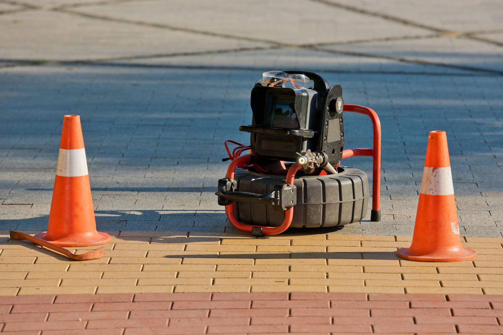 A machine is sitting on a brick sidewalk next to two orange cones.