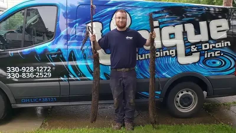 A man is standing in front of a van that says unique plumbing and drain inc.