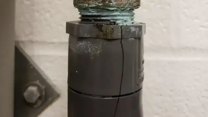 A close up of a cracked pipe against a white wall.