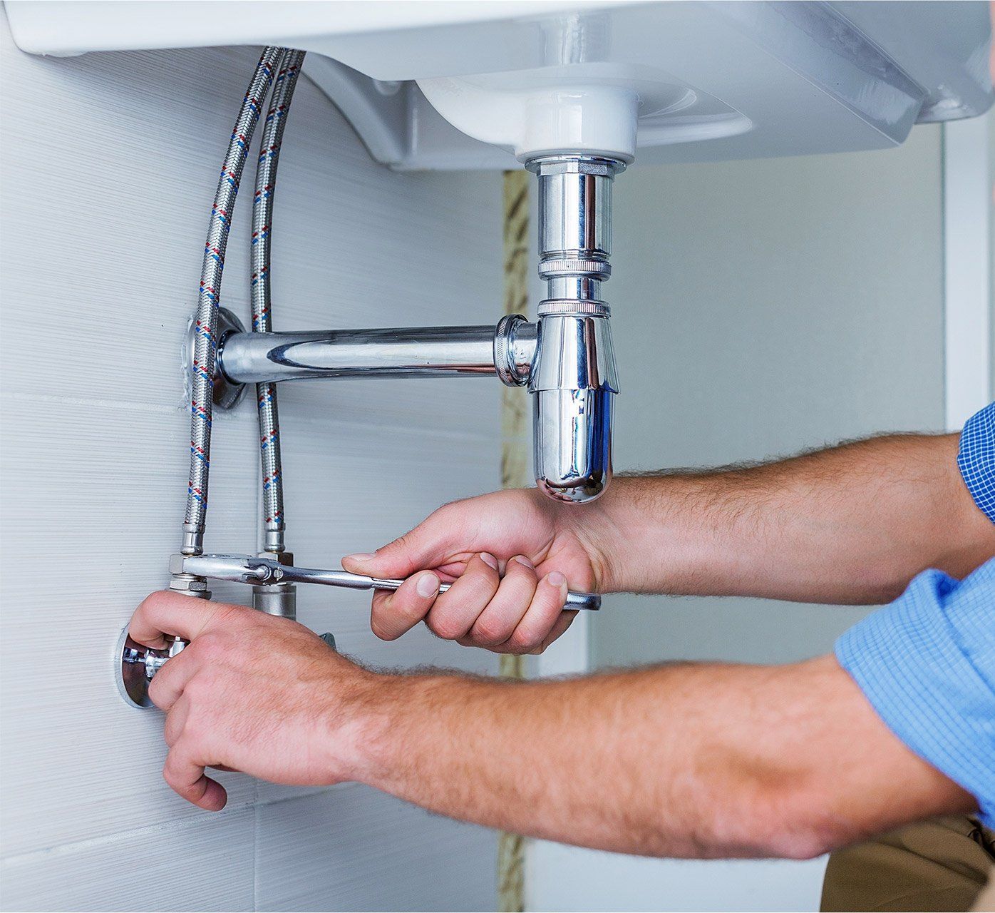 A man is fixing a sink with a wrench.