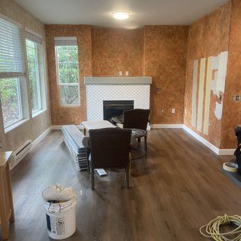 A living room with a fireplace , chairs , and a bucket of paint.