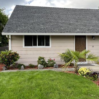 A small house with a gray roof and a large lawn in front of it.