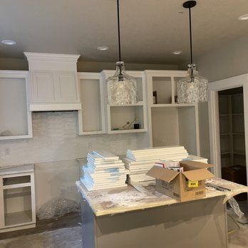A kitchen under construction with white cabinets and a cardboard box on the counter.