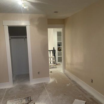 A room with beige walls and white trim is being painted.