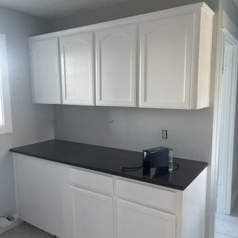 A kitchen with white cabinets and a black counter top.