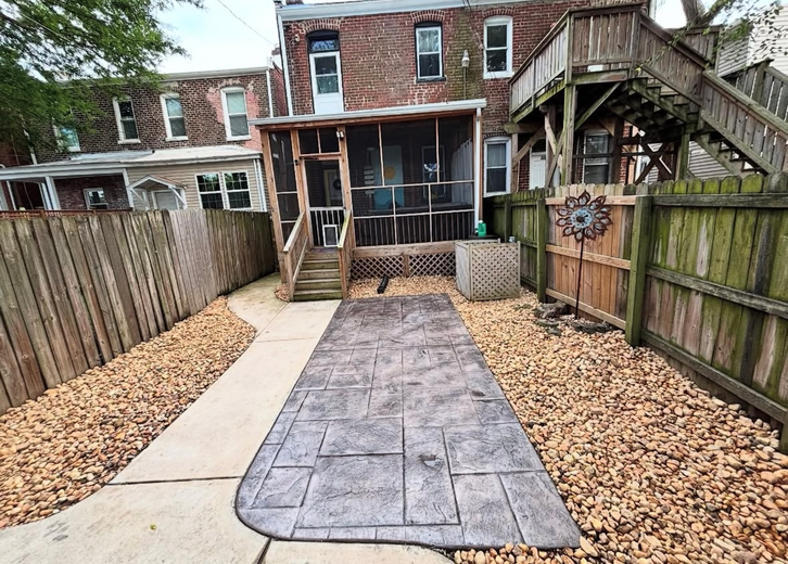 Backyard with a stamped concrete patio, screened porch, wooden fence, and gravel landscaping.