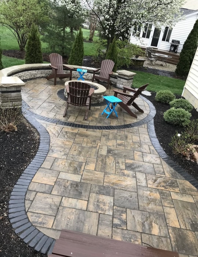 Patio with fire pit, seating, and pavers, surrounded by landscaping and lawn.