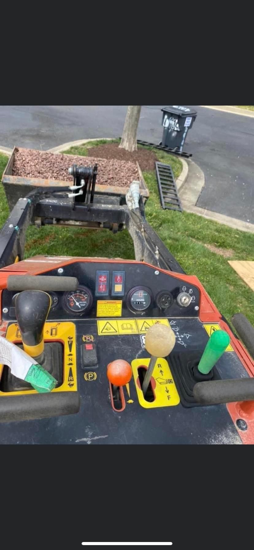 View from the operator's seat of a ditching machine, controls are in focus with a residential setting in the background.