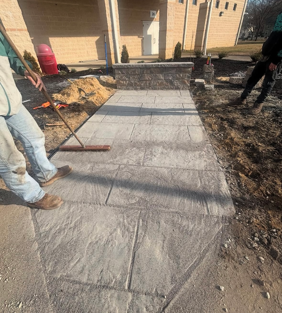 Workers paving a stone walkway leading to a building's entrance.