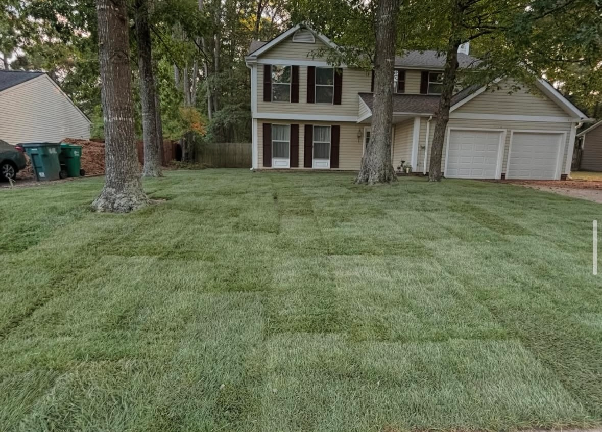 Two-story house with newly sodded lawn, trees, and two-car garage.