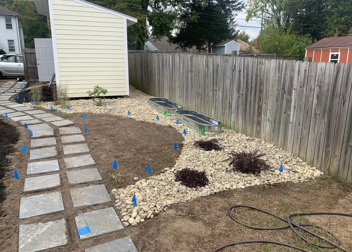 Stone path leads to a backyard garden with a wooden fence and shed.
