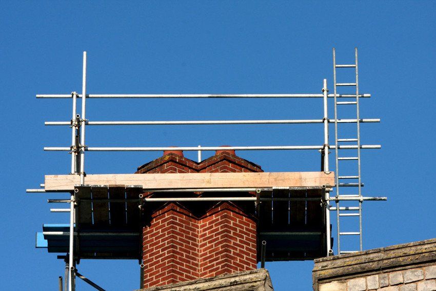 Man standing on rooftop of residential building to clean metal chimney of house with sweeper