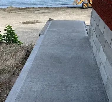 A concrete walkway leading to a beach with a bulldozer in the background.