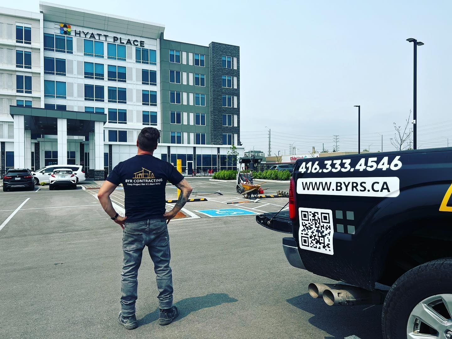 Man looking at a building with a black truck. The truck has a phone number and website on it. The building is a Hyatt Place.