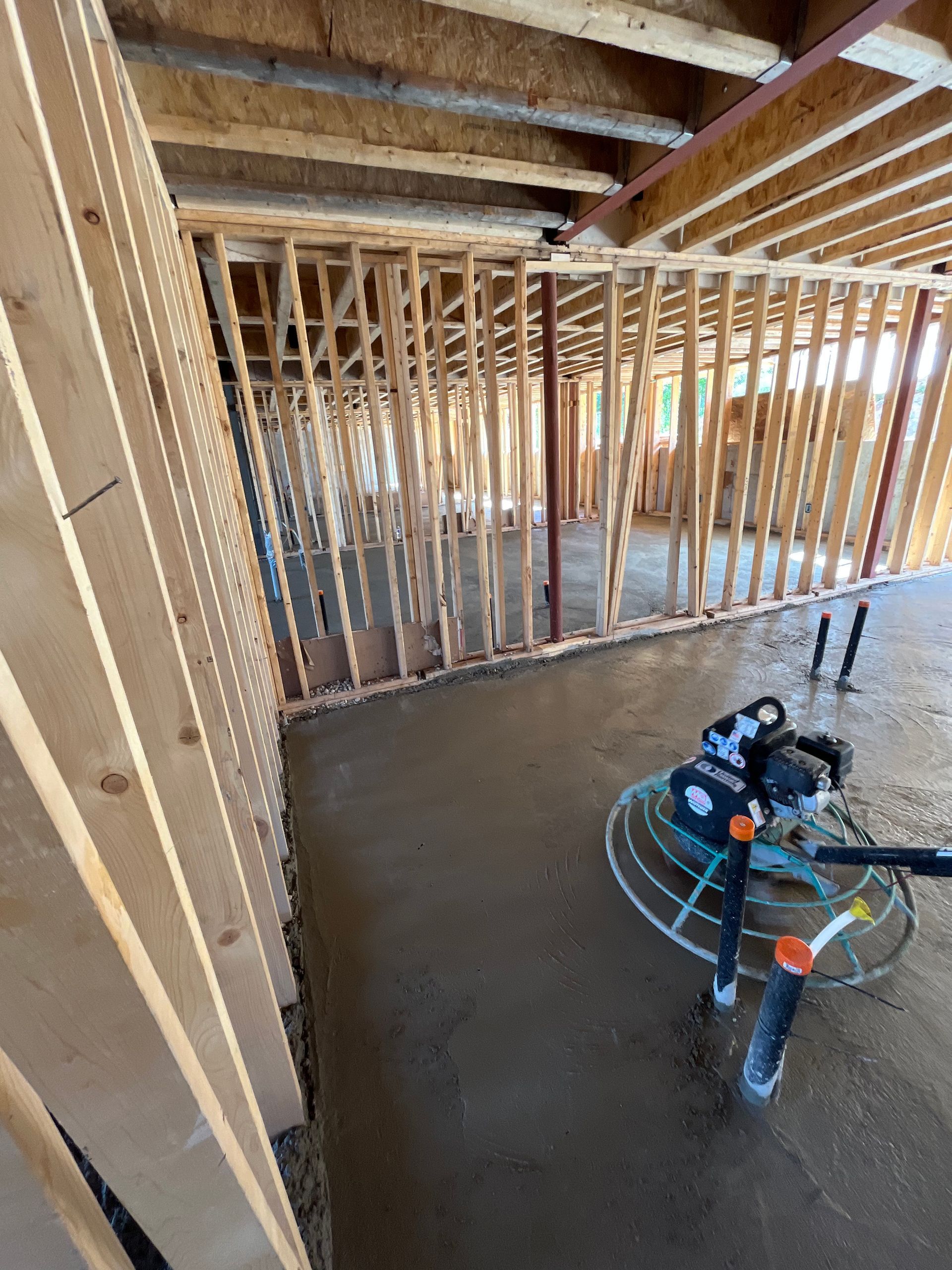 A machine is laying concrete in a room under construction.