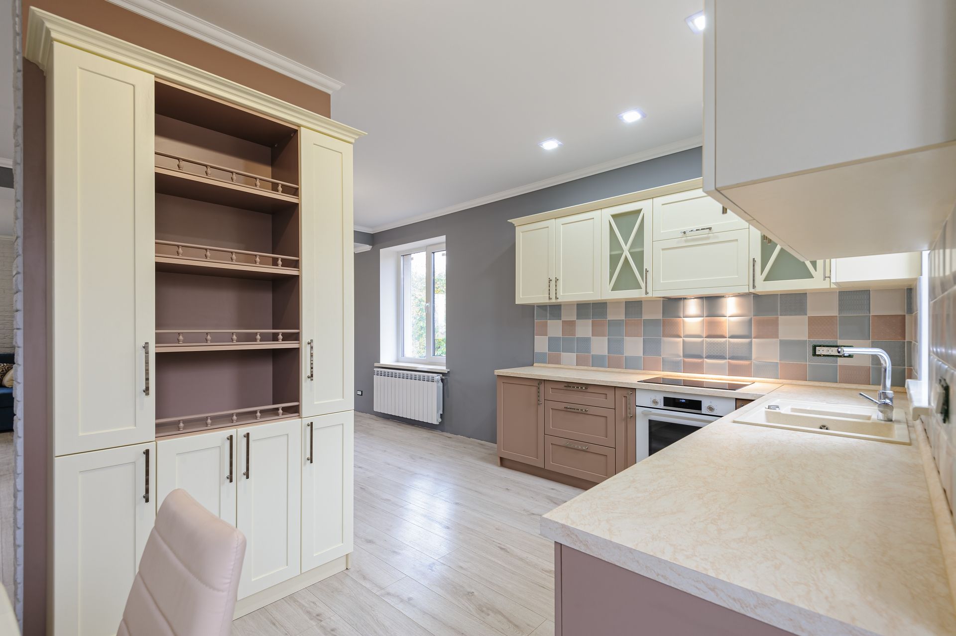 A kitchen with white cabinets , a stove , a sink and a chair.