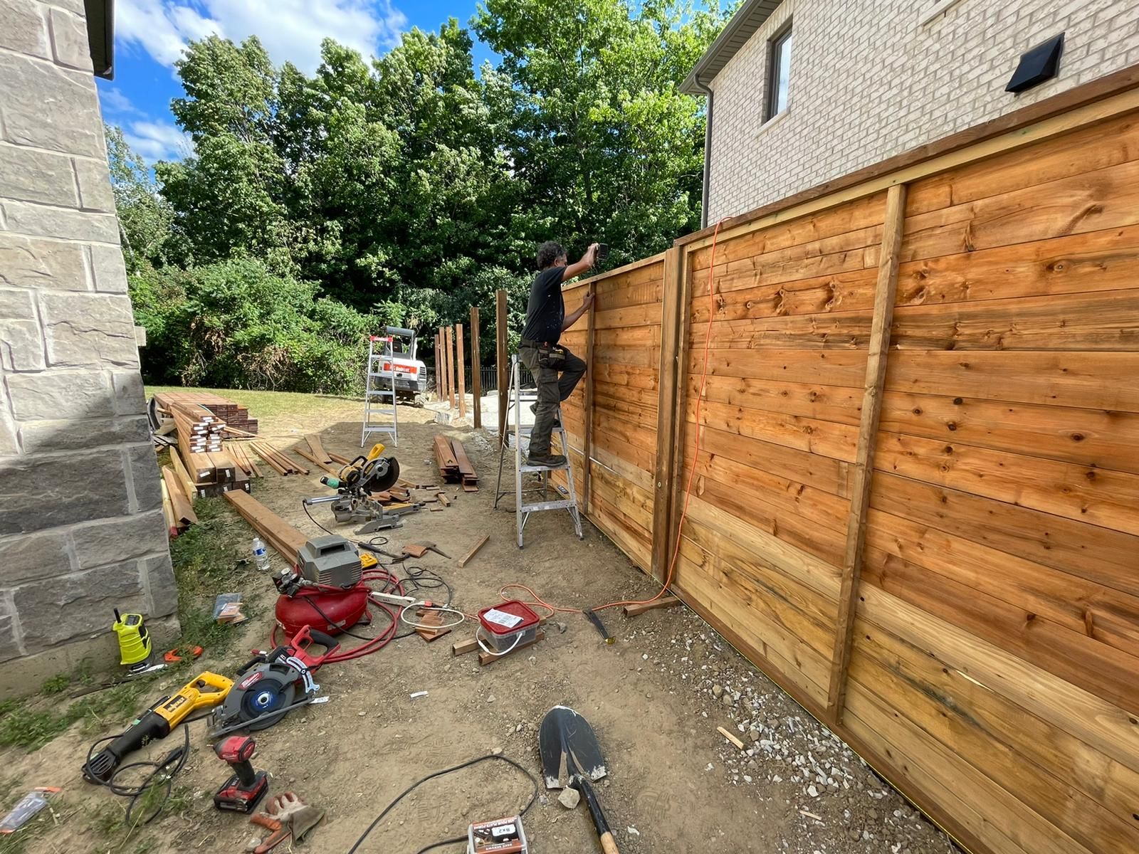 A man is standing on a ladder next to a wooden fence.